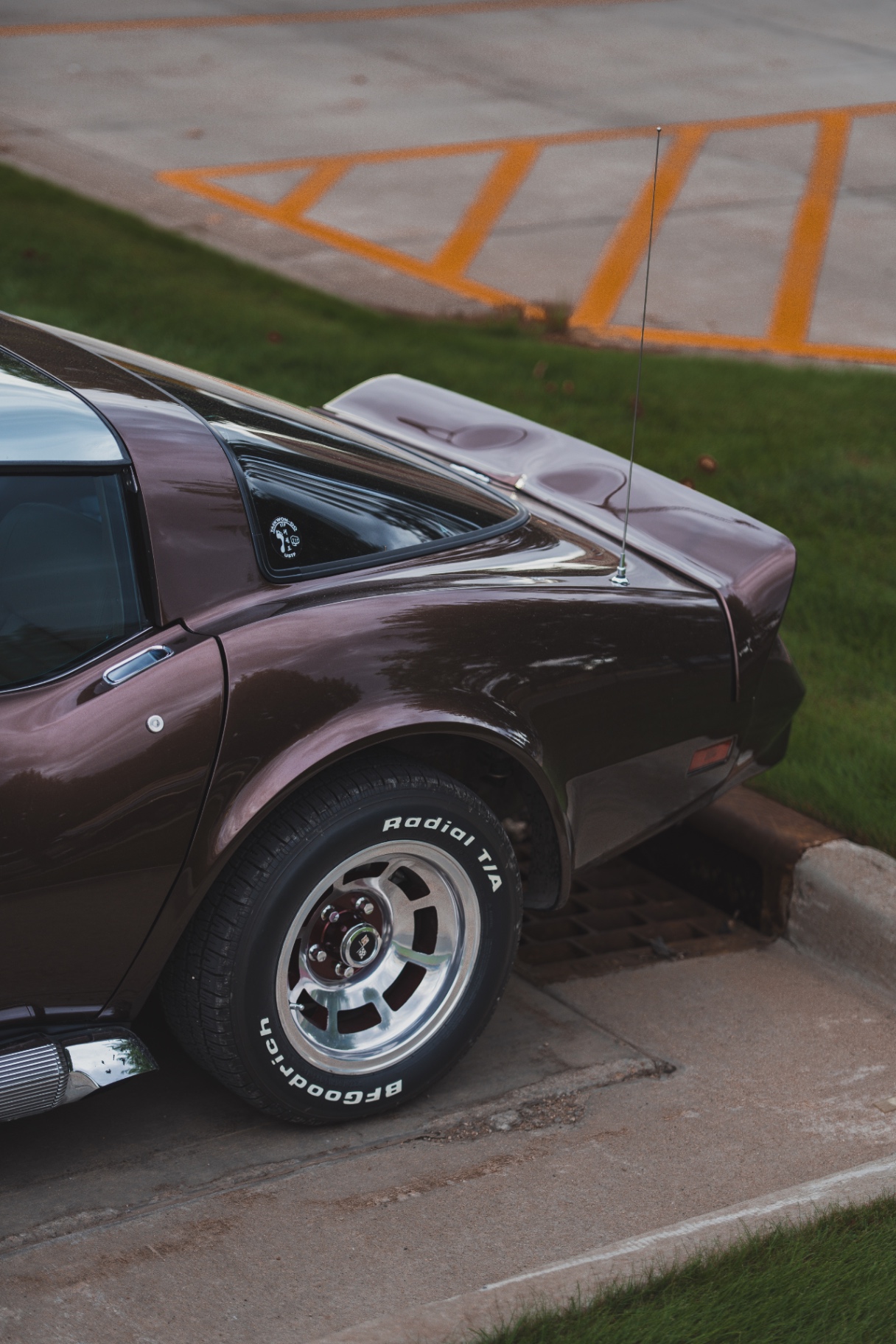 Rear quarter of a maroon C3 Corvette parked at a curb in evening light