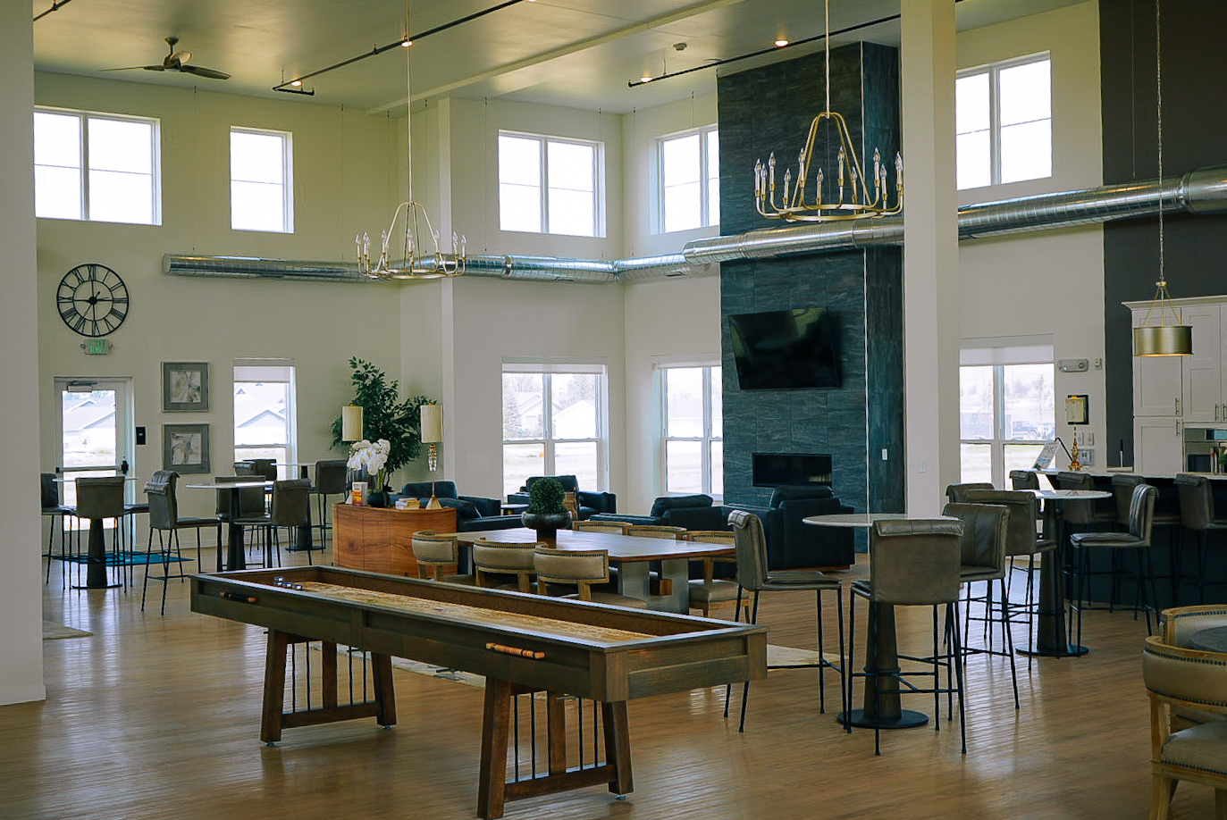Wide interior of a bright clubhouse lounge with shuffleboard, chandeliers and a stone fireplace