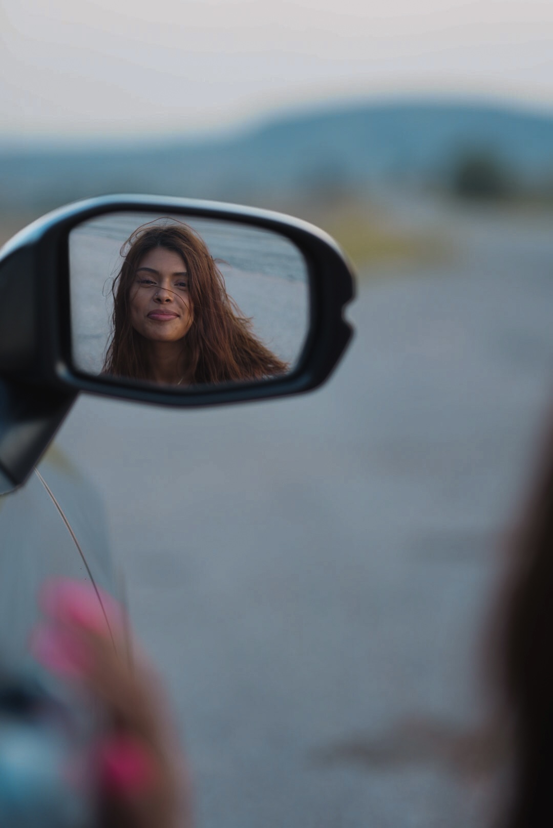 Woman's reflection in a car side mirror with wind in her hair at dusk