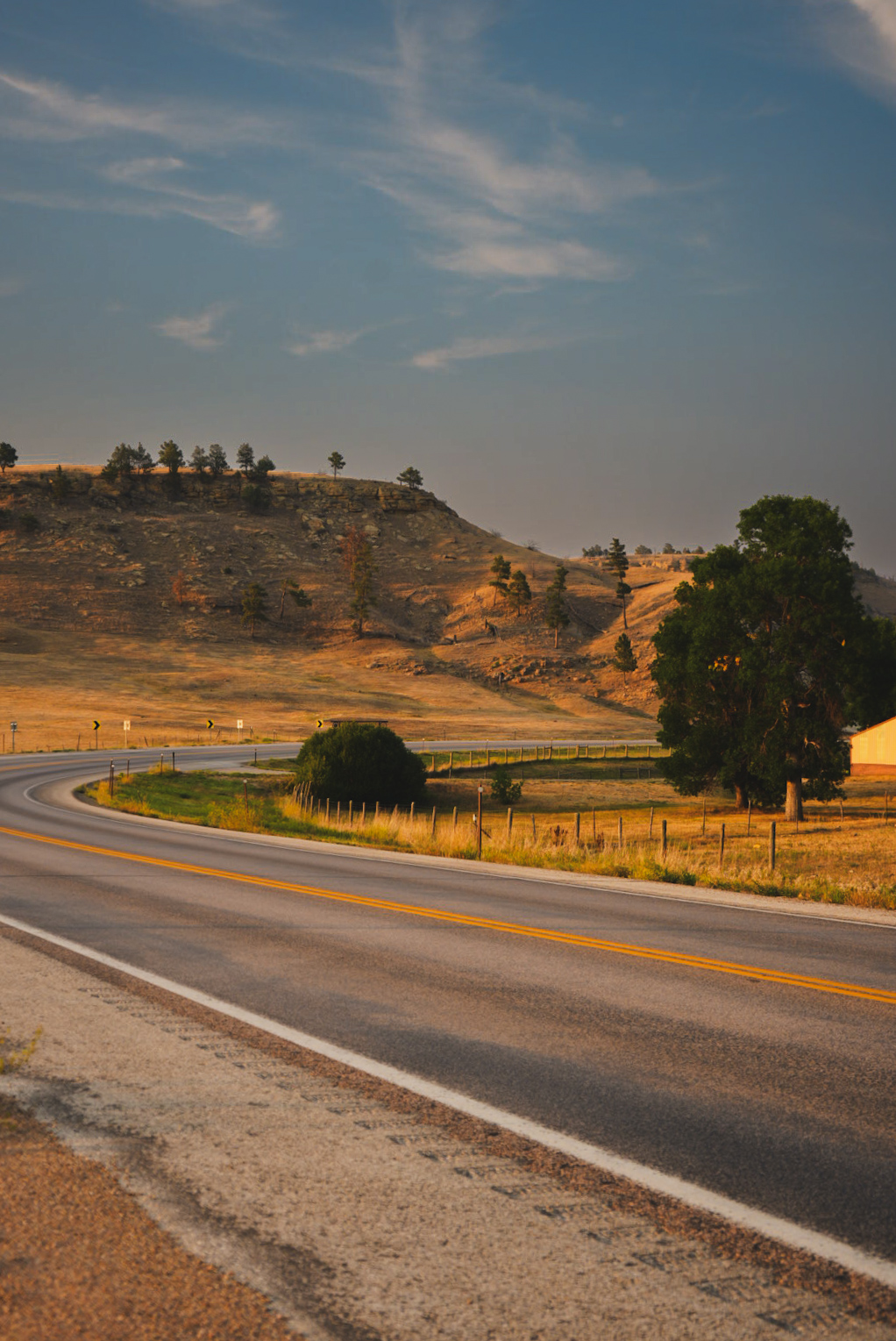 Empty two-lane highway curving past golden bluffs in warm evening light