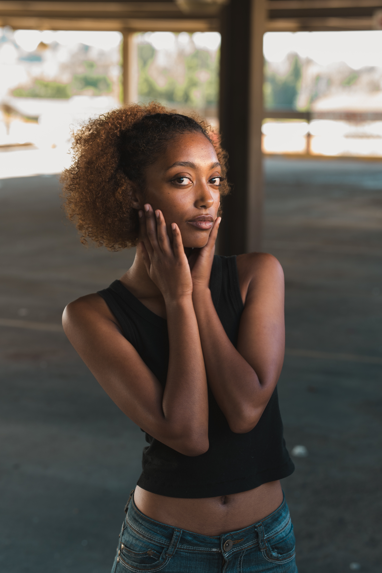 Woman resting her hands against her face in soft daylight inside a parking structure