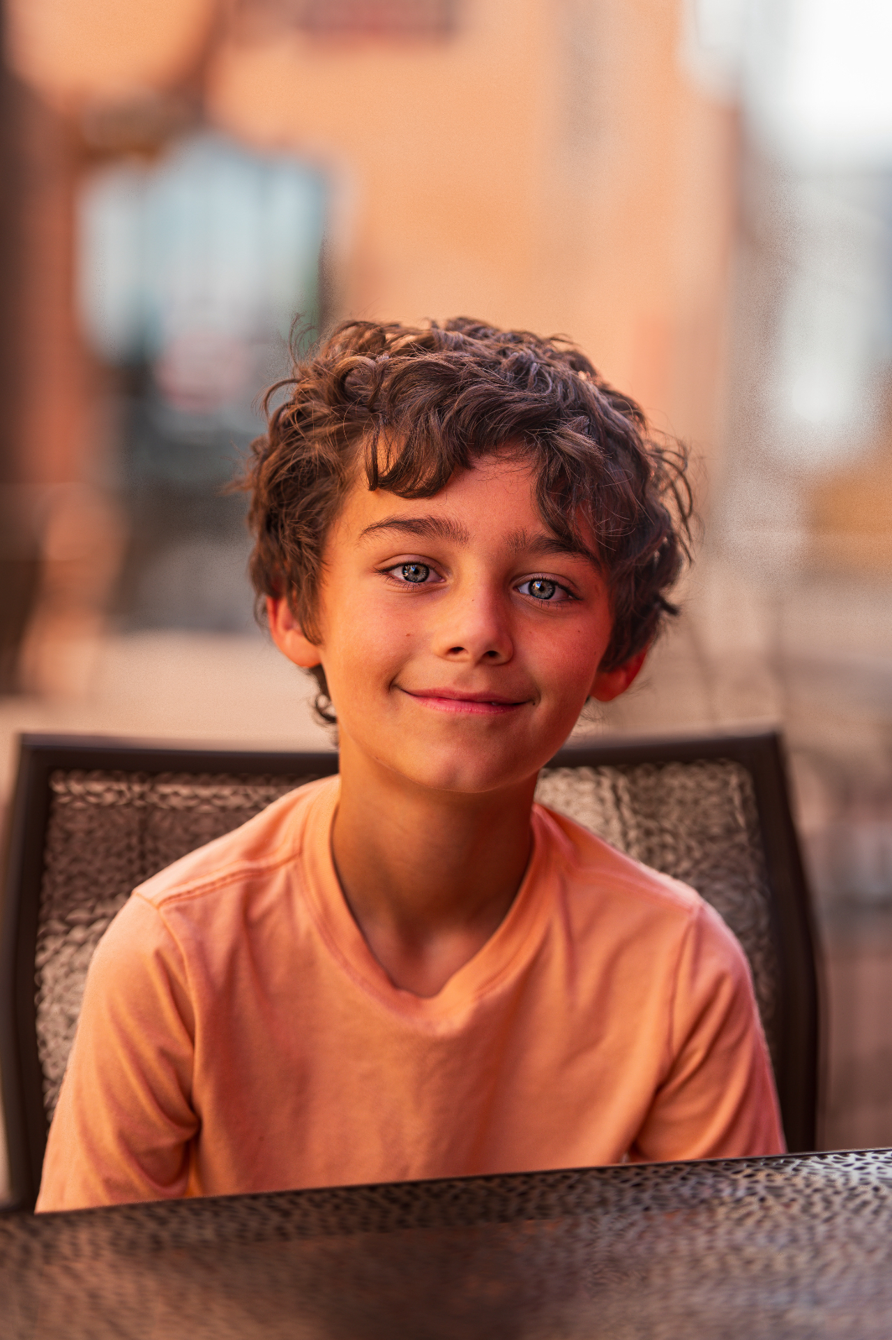 Young boy with curly hair smiling at an outdoor table in warm sunset light