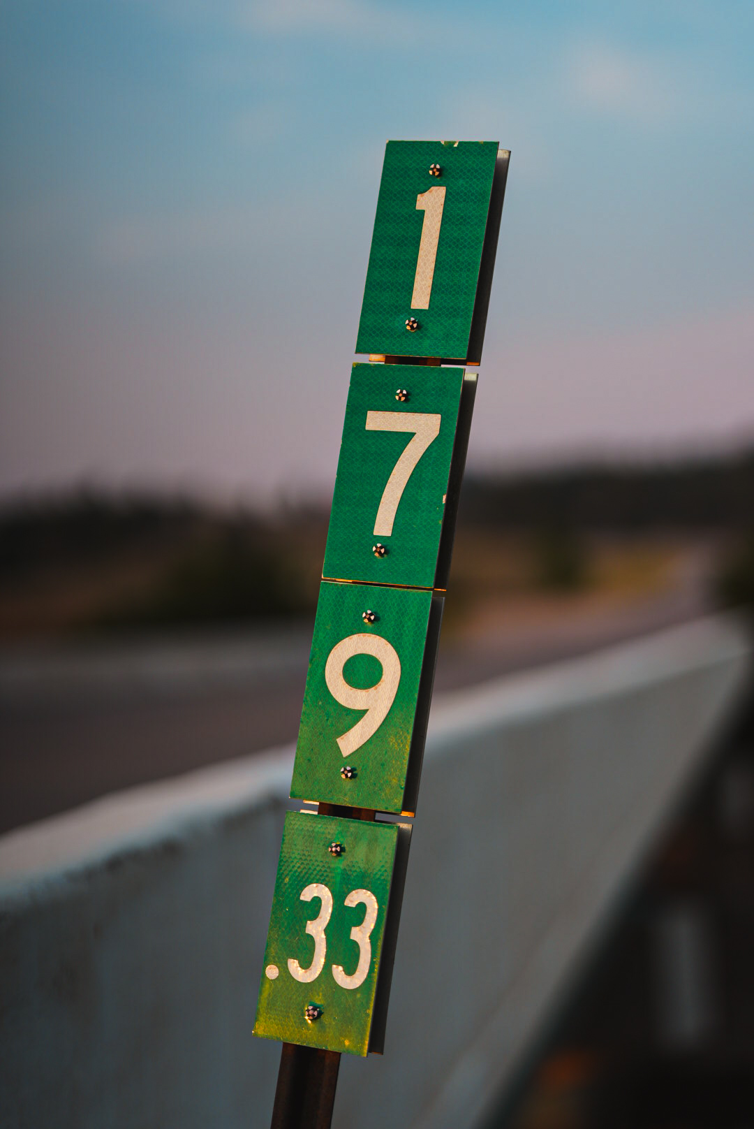 Green highway mile-marker sign on a bridge rail at twilight