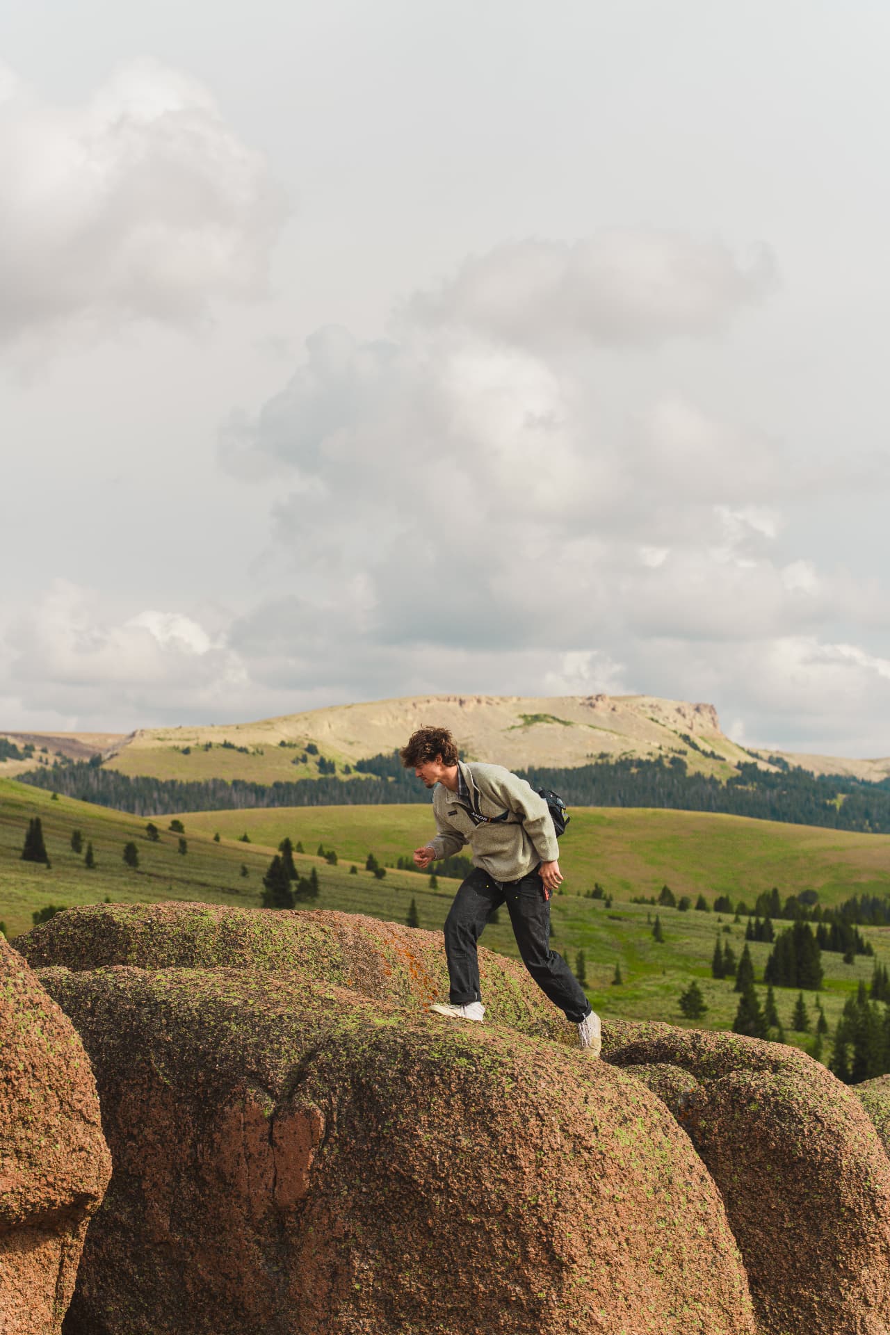 Man stepping across rocks with rolling green mountains behind him