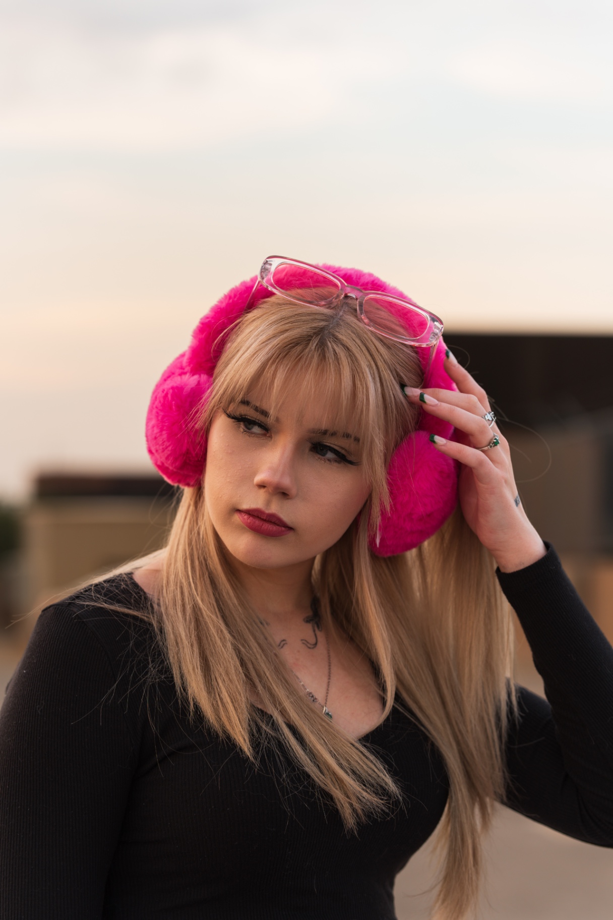 Blonde woman in hot pink fuzzy earmuffs and pink sunglasses at sunset