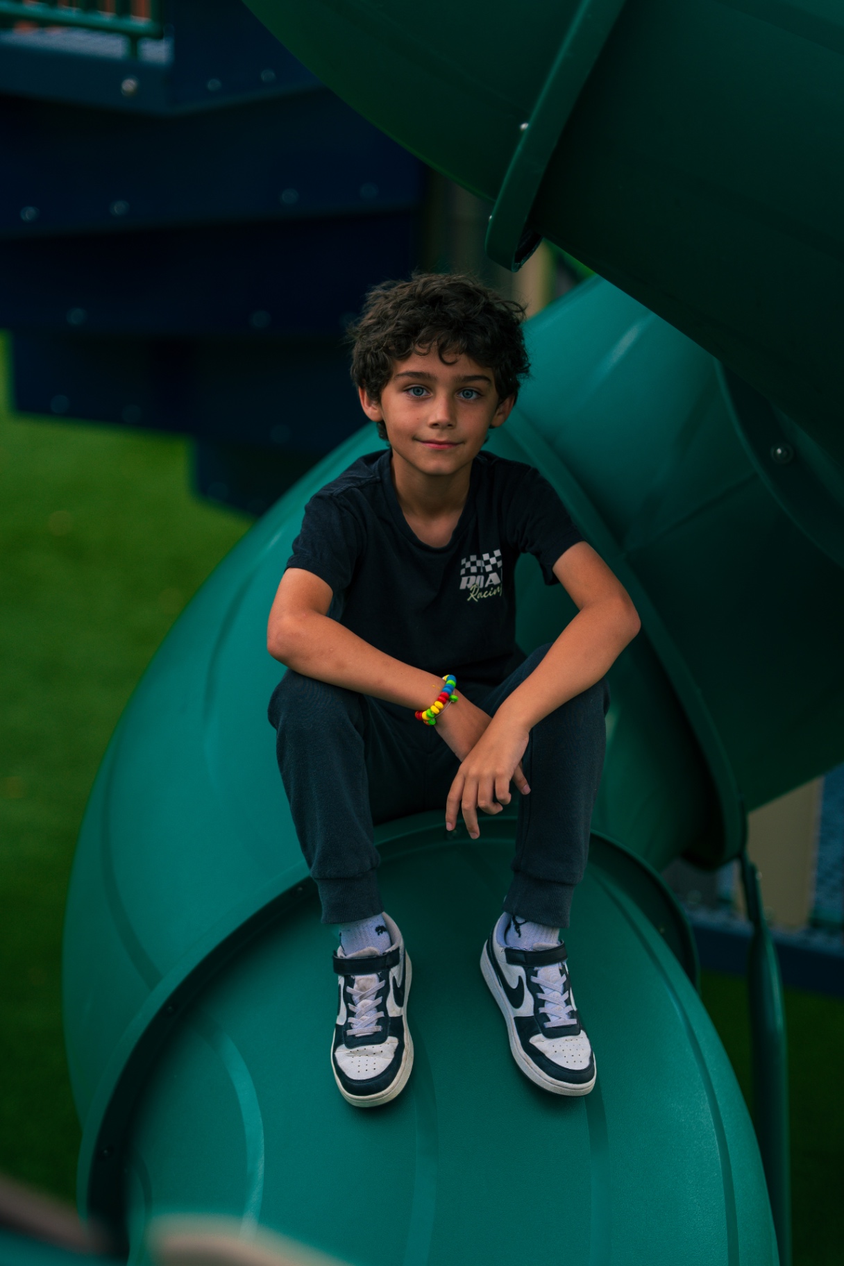 Boy sitting on a green playground slide smiling at the camera