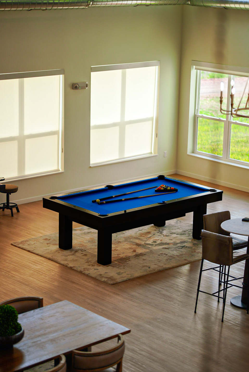 Blue-felt pool table in a sunlit community game room with hardwood floors