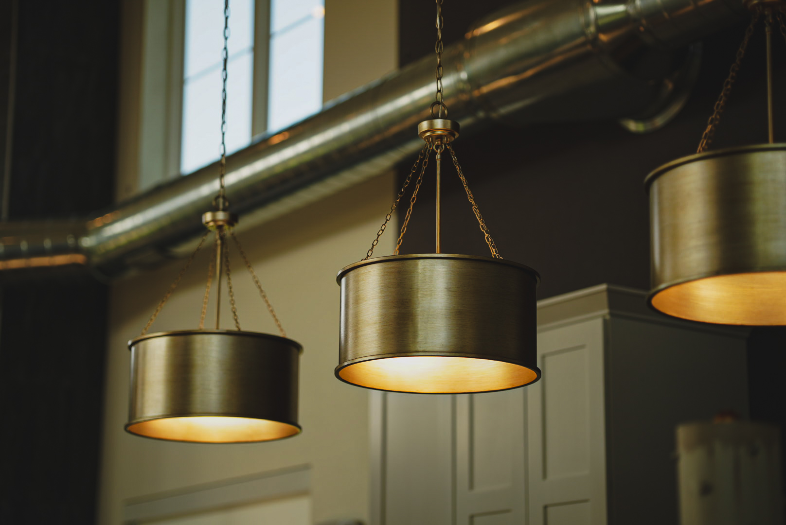 Row of brushed brass pendant lights glowing against exposed ductwork