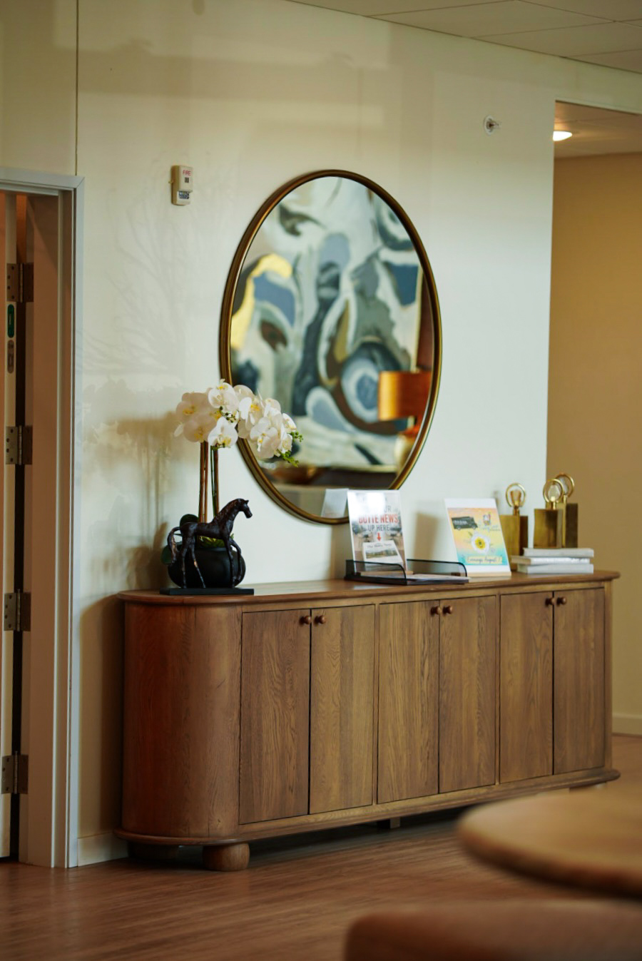 Wood credenza with round mirror, orchids and brochures in an apartment entry