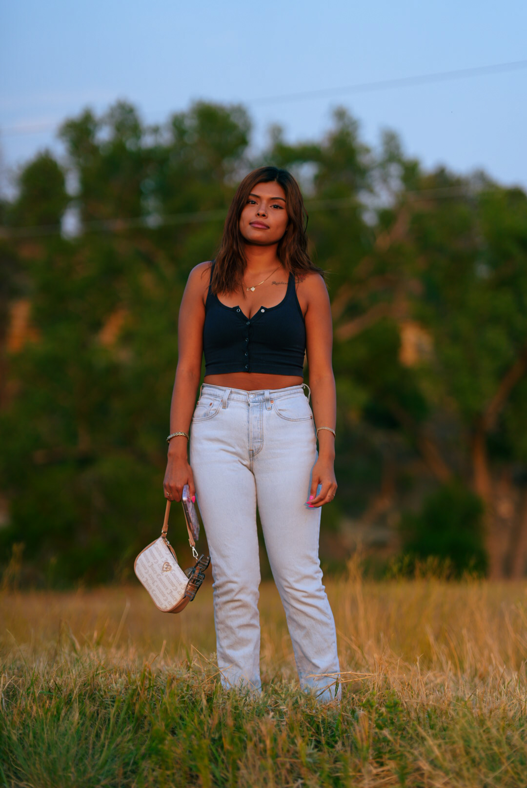 Woman standing in a grass field at blue hour holding a small shoulder bag