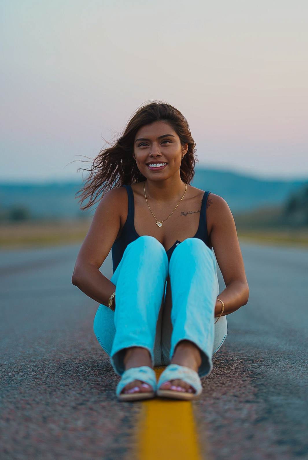 Woman seated on the yellow centerline of an empty highway at dusk