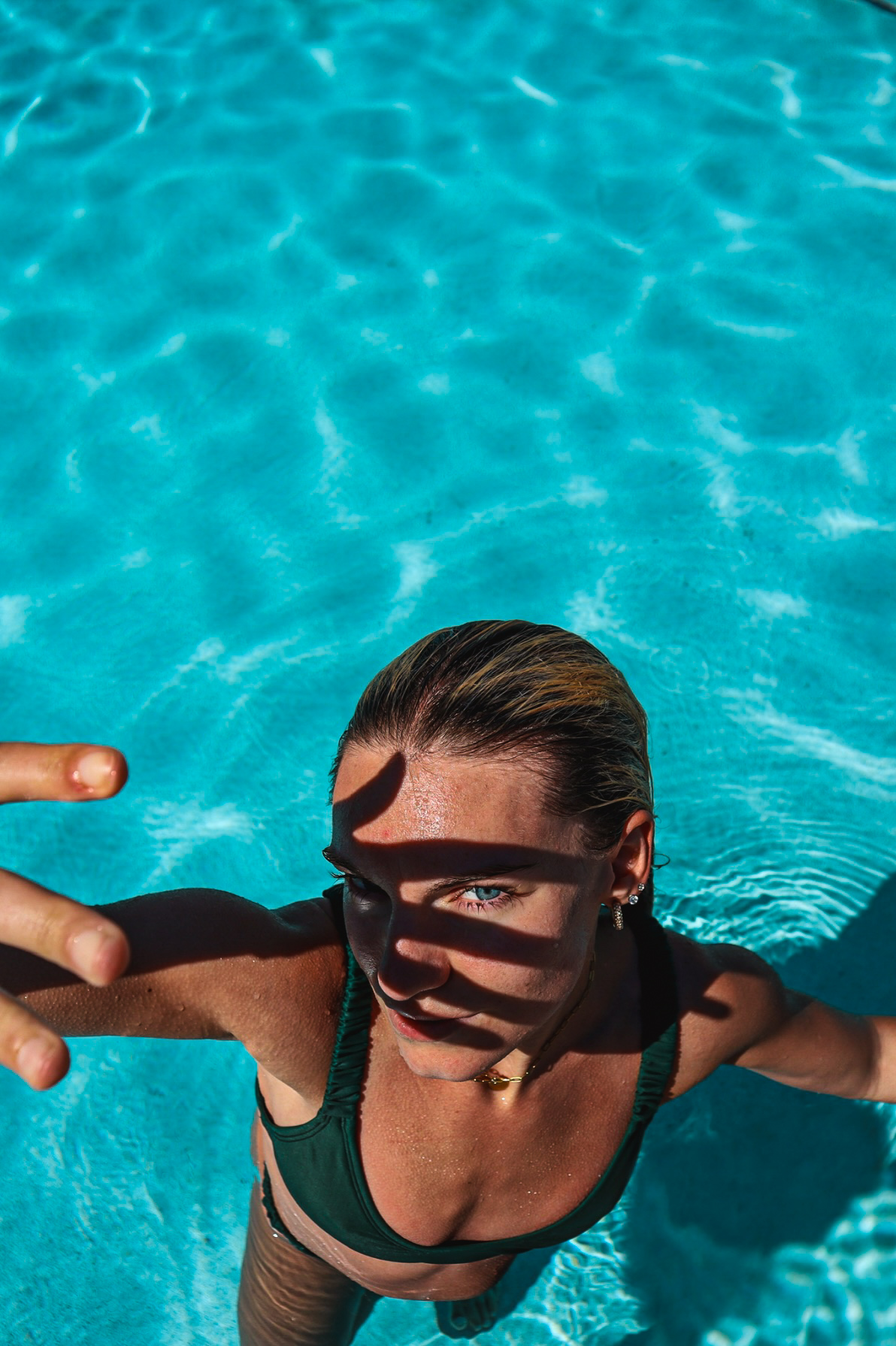 Overhead portrait of a woman standing in a turquoise pool shading her eyes