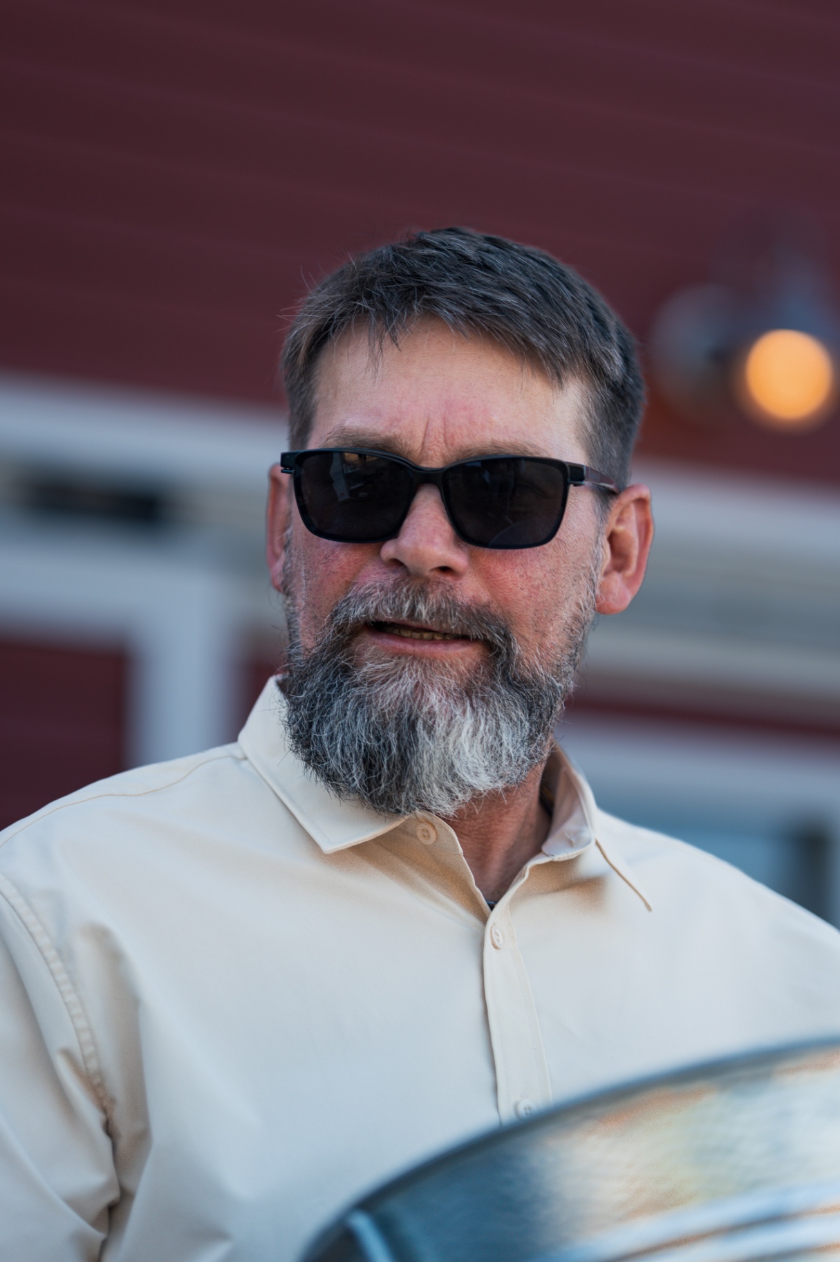Man with a gray beard wearing sunglasses and a cream shirt outdoors