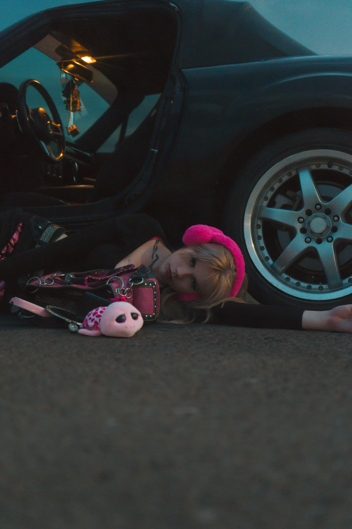 Low-angle portrait of a woman resting on the pavement beside a car wheel
