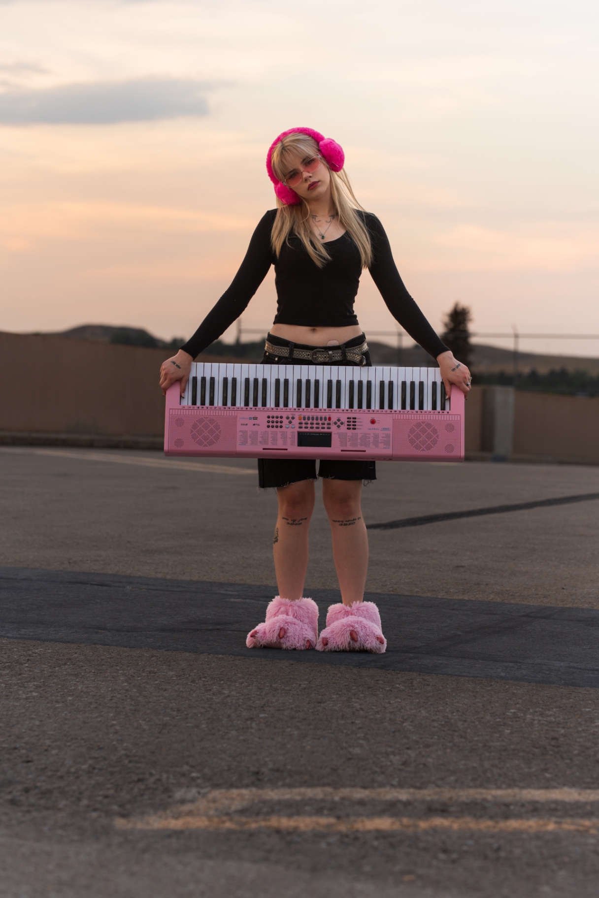 Woman holding a pink keyboard standing on a rooftop parking deck at sunset