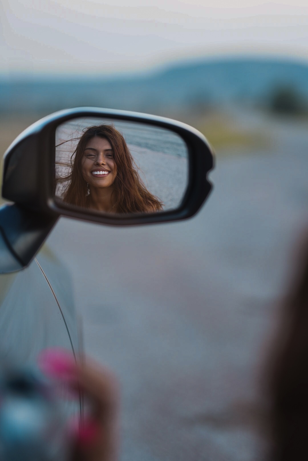Woman laughing reflected in a car side mirror on an open road