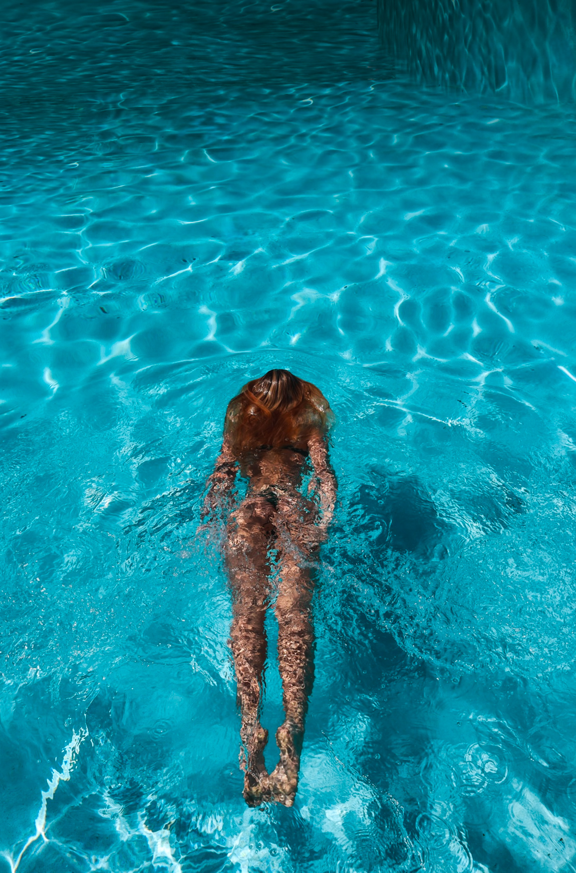 Overhead view of a swimmer gliding through bright blue pool water