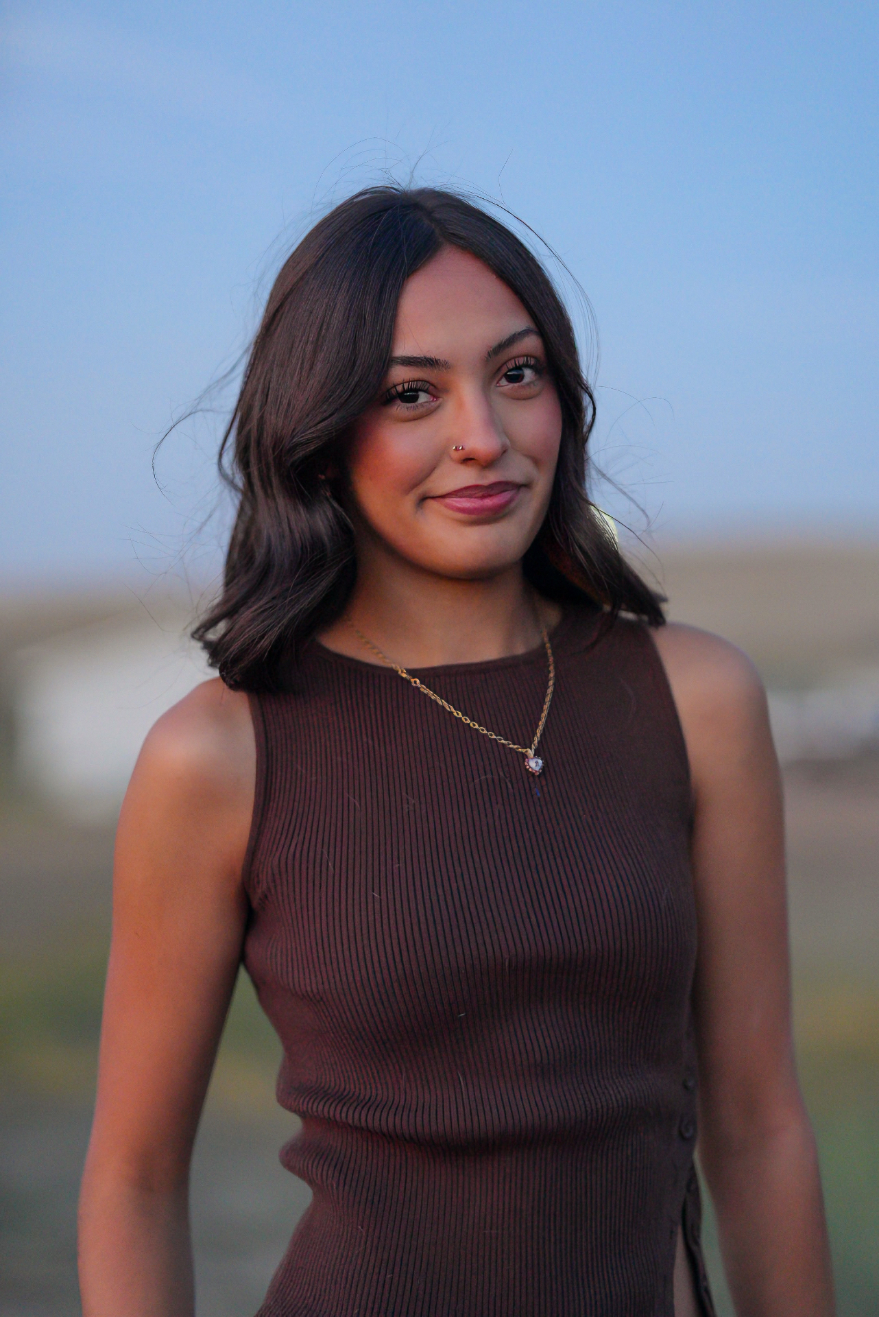 Senior portrait of a young woman in a brown knit top against a blue dusk sky