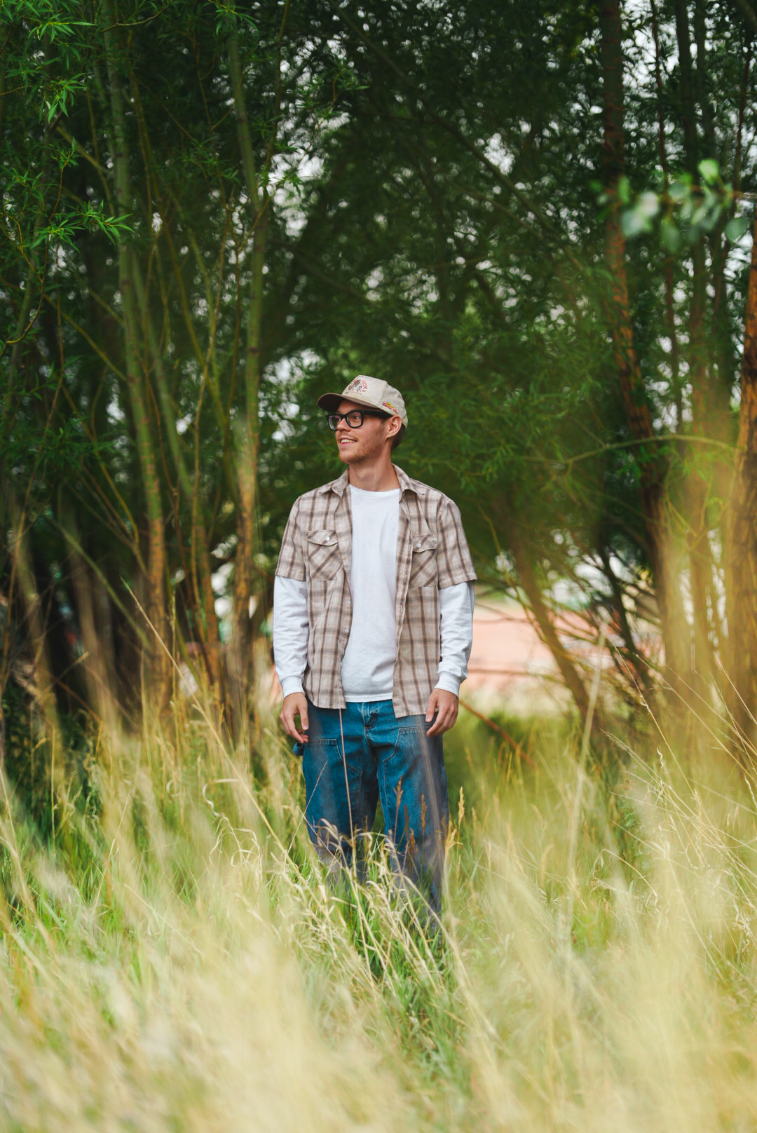 Man in a plaid shirt standing among willow trees and tall summer grass