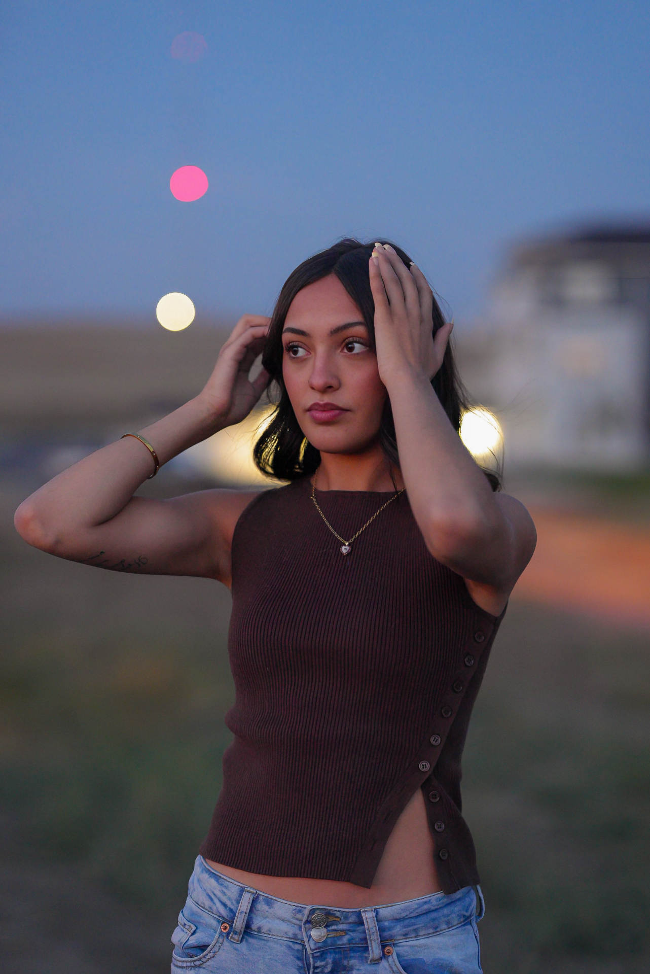 Young woman brushing back her hair at blue hour with colorful bokeh lights behind her