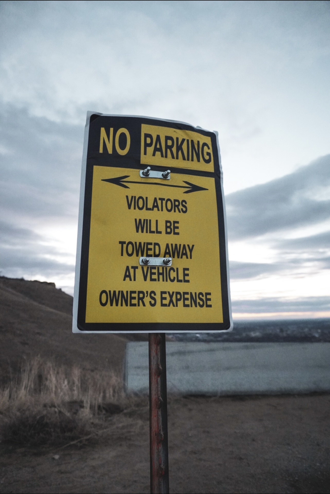 Yellow no-parking sign on a bluff above a river at dusk
