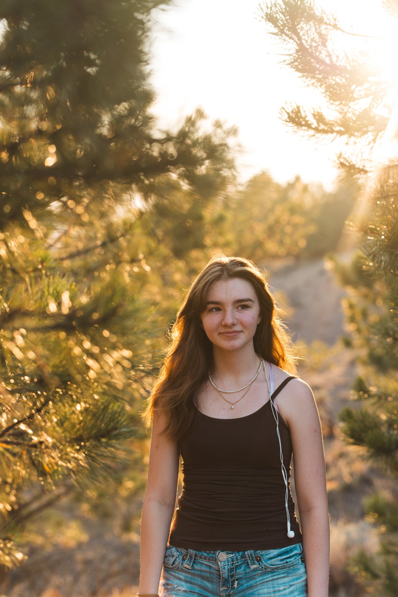 Portrait of a young woman backlit by golden sunlight among pine trees