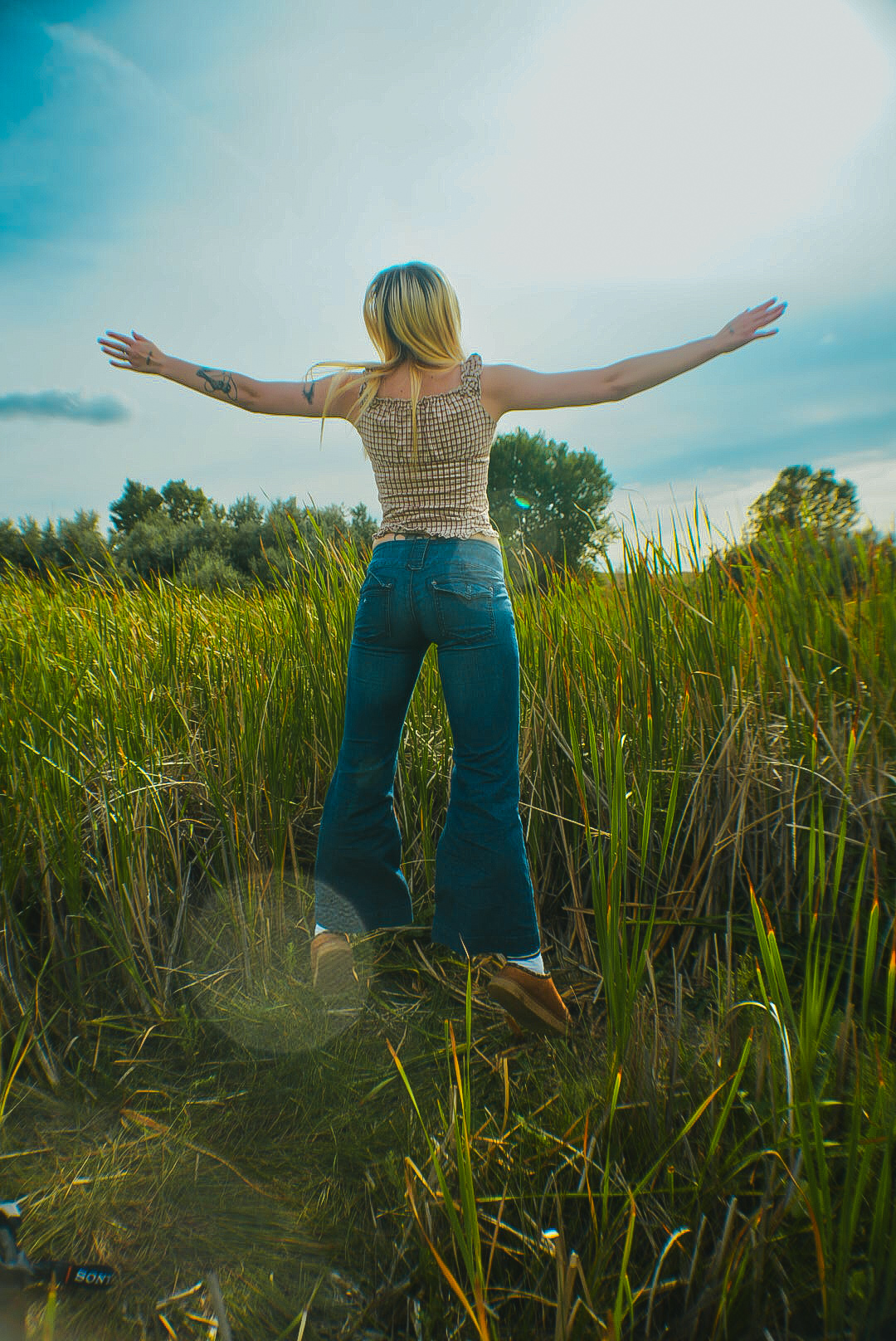Woman standing in tall marsh grass with arms outstretched toward the sky
